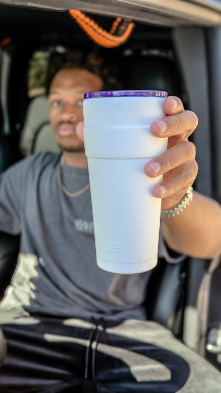 A white Sippers Only with a purple lid held toward the camera