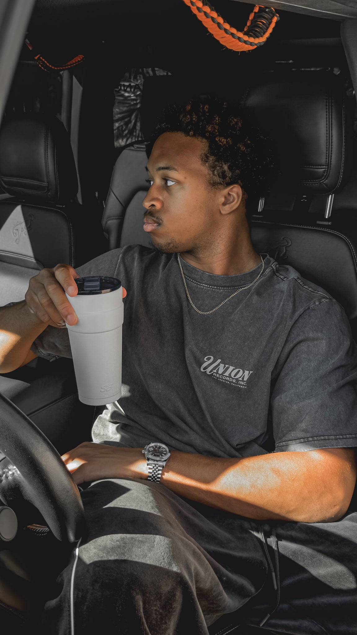 A man seated in a car holding a white Sippers Only tumbler